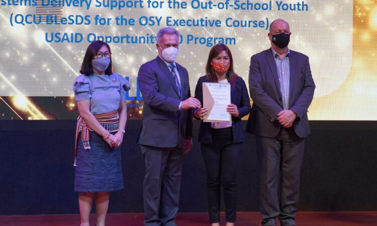 From left: QCU President Dr. Theresita Atienza, USAID Philippines Education Director Dr. Tom LeBlanc, and USAID Opportunity 2.0 Chief of Party Dr. David Hall award a certificate of completion to Barangay Culiat Kagawad Marichu Montehermoso (second from right) during the closing ceremonies of the “Executive Course for Barangay Leaders on System Delivery Support for OSY” program on July 26.