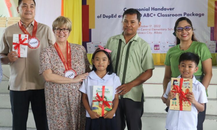 USAID Deputy Assistant Administrator LeAnna Marr (second from left) and DepEd Region V Director Gilbert Sadsad (leftmost) lead the handover of classroom reading materials for early grade learners at Tabaco North Central Elementary School, Albay.