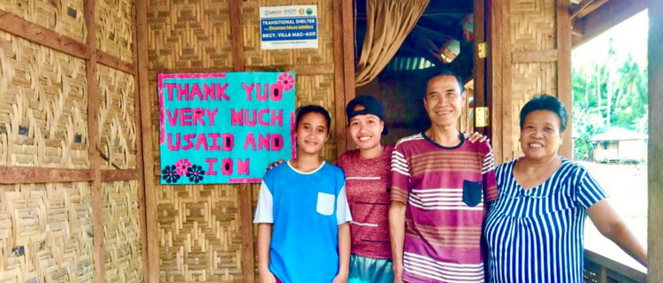 Four people standing by the entrance of a transitional shelter.