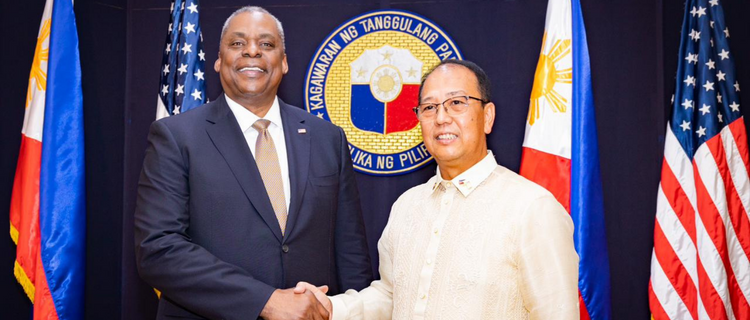 Secretary of Defense Lloyd J. Austin III shaking hands with Secretary Carlito Galvez Jr., Officer-in-Charge of the Philippine Department of National Defense (DND) in front of U.S. and Philippine flags and the DND seal.