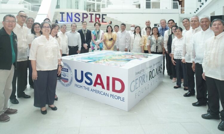Ambassador Carlson and representatives of organizations awarded grants by USAID Philippines stand around an installation showing the USAID and Gerry Roxas Foundation logos. Behind them are large letters that spell "INSPIRE."