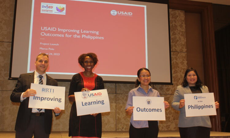 Four people holding signages with words forming the program name "Improving Learning Outcomes - Philippines."