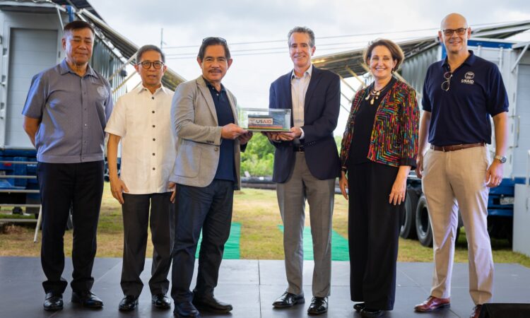 National Power Corporation President and CEO Fernando Roxas and USAID Philippines Mission Director Ryan Washburn hold a miniature replica of a USAID mobile energy system (MES) in the presence of Philippine Department of Energy (DOE) Secretary Raphael Lotilla, U.S. Ambassador MaryKay Carlson, DOE Undersecretary Giovani Bacordo, and USAID Philippines Environment Office Director Ryder Rogers.